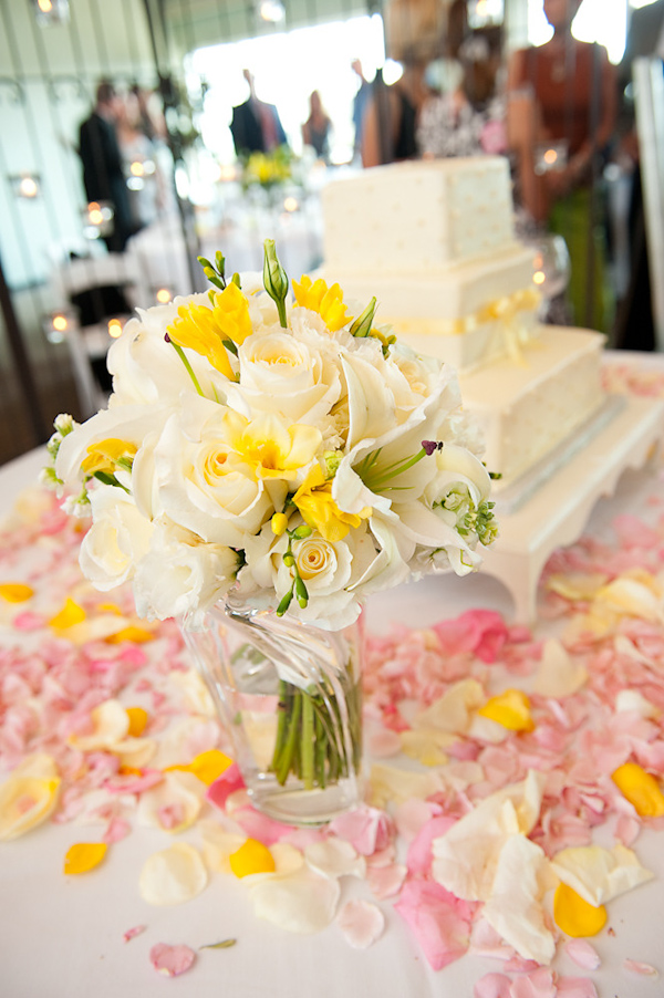 photo of the cake table decorated with a white tablecloth covered with ivory, pink, and yellow rose petals, and the bride's yellow, white, and green bouquet sitting in a vase - photo by Houston based wedding photographer Adam Nyholt 